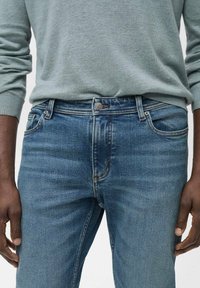 Lichtblauwe denim jeans met een aansluitend ontwerp, vijf zakken en een metalen knoopsluiting. Enige vervaging en subtiele stikseldetails.