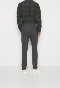 Gråternede bukser med slim fit, elastisk talje, sidelommer og en enkelt baglomme, parret med en grønternet skjorte.