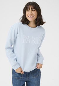 Ljusblå sweatshirt med "PARIS" broderat i vitt. Har rundad halsringning och ribbade muddarna. Kombineras med blå jeans. Mjuk textur.