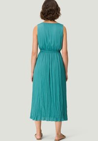 Teal ærmeløs kjole med indsamlet talje, flydende tekstur og ankel længde, der har et let plisseret design.