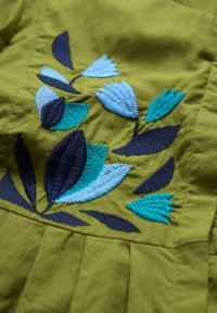 Vyšívaný design s modrými a námořnickými listy na olivově zelené látce, ukazující texturu a detaily v prošití.