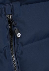 Marineblå dunjakke materiale, med en sort glidelås og teksturert drahank med logo. Glatt stoff med en lett glans.