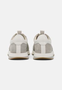 Grå semsket sneakers med en glatt hvit lærsåle, en teksturert bakre flik og en gummisåle. Har subtile tonale aksenter og sømmer.