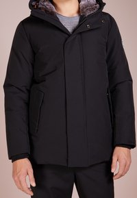 Czarna kurtka puchowa z podszewką w kapturze, zapięcie na zatrzaski i zamek błyskawiczny, boczne kieszenie i ściągacze na mankietach. Gładka tekstura i minimalistyczny design.
