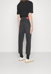 Jeans in denim neri con una vestibilità rilassata, risvoltati alle caviglie, caratterizzati da un'etichetta arancione sul retro. Accoppiati con sneakers bianche e calzini neri.