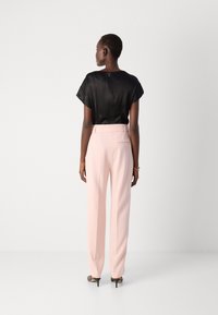 Top in satin nero con maniche a farfalla corte e zip sul retro. Pantaloni su misura rosa chiaro con vestibilità slim e dettaglio della tasca posteriore.