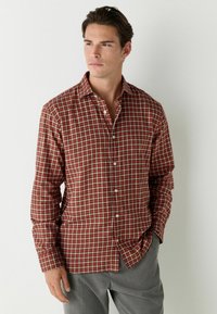 Chemise à carreaux rouge et marron en tissu léger, dotée d'un col, d'une fermeture avant à boutons complète et de manches longues avec des poignets boutonnés.