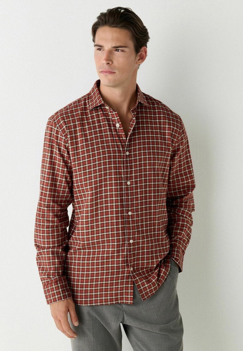 Chemise à carreaux rouge et marron en tissu léger, dotée d'un col, d'une fermeture avant à boutons complète et de manches longues avec des poignets boutonnés.