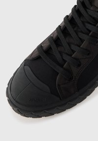 Baskets noires présentant un mélange de cuir lisse et de nylon texturé. Bout arrondi avec semelle en caoutchouc et lacets épais pour un maintien sécurisé.