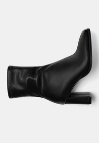 Bottine noire à laçage ajusté avec un design effilé, en cuir lisse, et un talon carré épais. Présente une tige ajustée et plissée.