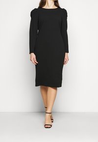 Svart långärmad klänning med en figursydd silhuett, rund halsringning och puffärmar. Tyget ser slätt ut med en liten stretch.