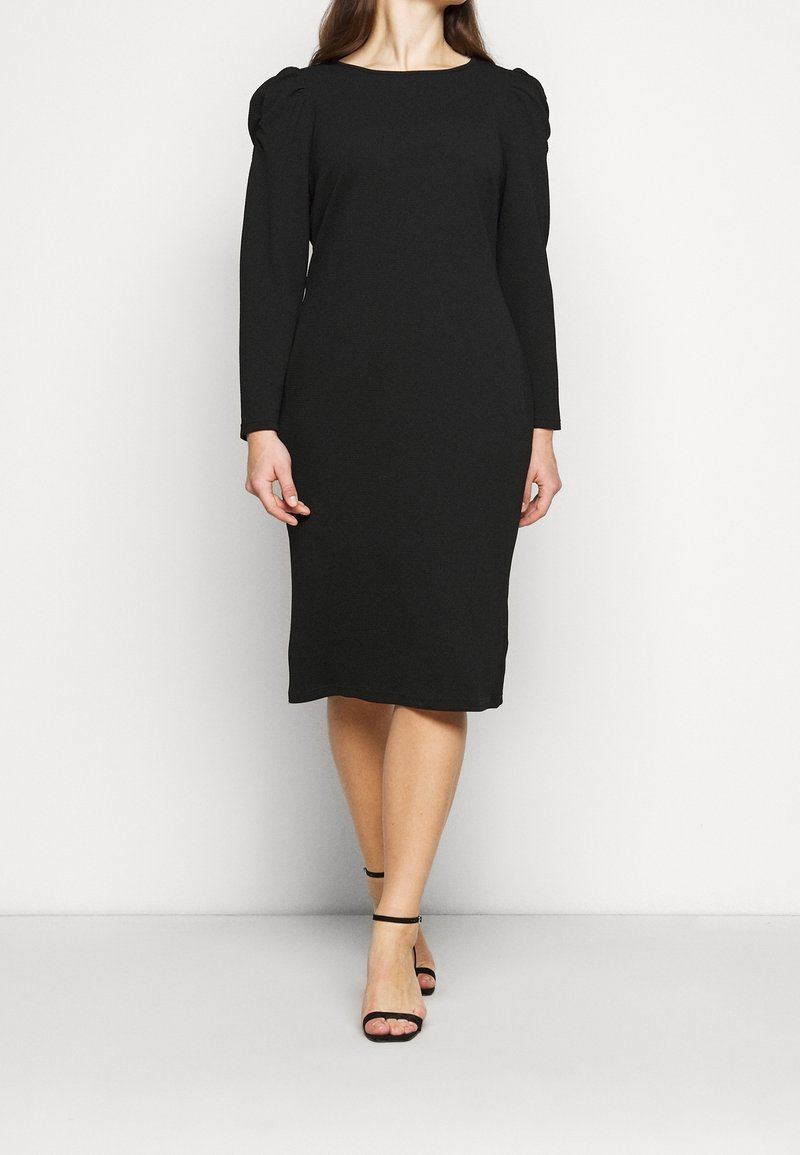 Svart långärmad klänning med en figursydd silhuett, rund halsringning och puffärmar. Tyget ser slätt ut med en liten stretch.