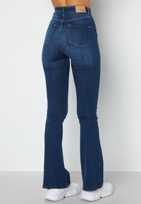 Hoge taille denim flared jeans in donkerblauw met een soepele textuur, voorzien van achterzakken en een subtiel merklabel op de tailleband.