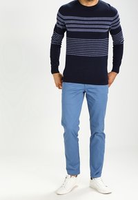 Pull en maille bleu marine à rayures horizontales bleues, associé à un pantalon bleu clair et des baskets blanches. Il présente un col rond et des manches longues.