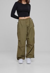 Zkrácený černý top s dlouhým rukávem spárovaný s volnými olivově zelenými kalhotami, které mají elastický pas, šňůrkové detaily a boční kapsy. Bílé tenisky.