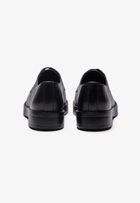 Black leather shoes with a smooth finish, rounded toe, low heel, and elastic side panels for easy slip-on access. Minimalist design.
