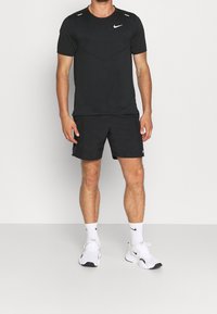 Czarna sportowa koszulka Nike z krótkim rękawem, zestawiona z pasującymi czarnymi szortami. Biały logo Nike na koszulce i butach; skarpetki są białe.