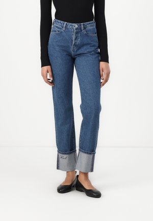 High-waisted blue denim jeans with a straight cut, featuring contrasting fabric cuffs and an embroidered logo on the hem.