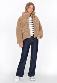 Beige, fluffy, kravecropped jakke med en boksformet silhouette. Kombineret med en stribet skjorte, mørke denimbukser og hvide sneakers.