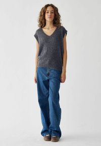 Top gris sin mangas en una tela suave; combinado con jeans azules de corte holgado y zapatos marrones; diseño simple, sin patrones o acentos visibles.