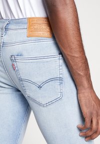 Vaqueros ajustados de mezclilla en azul claro con un acabado texturizado, que presentan un diseño clásico de bolsillo trasero y una etiqueta de cuero marrón en la cintura.