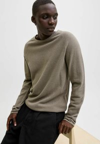 Stickad tröja med långa ärmar i dämpad beige färg med rund halsringning och strukturerat tyg; kombinerad med svarta byxor i avslappnad passform.