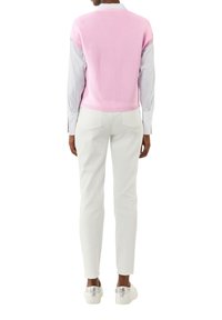 Różowy sweter z dzianiny o teksturowanym wykończeniu, noszony na białą koszulę, w połączeniu z białymi spodniami o wąskim kroju i sneakersami z srebrnymi akcentami.
