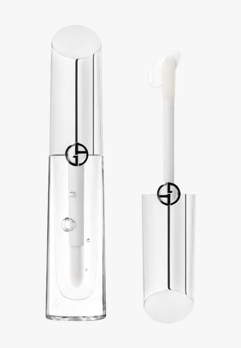Envase de brillo labial transparente con una tapa plateada brillante, que presenta un cuerpo transparente y un aplicador blanco. Detalle del logo en negro visible.