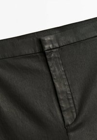 Svart tyg med en slät textur, med en dold dragkedja och en rak söm vid midjan, vilket ger ett snyggt utseende.