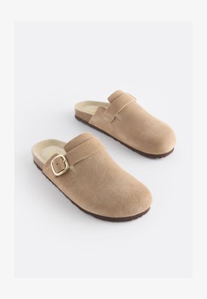Bézs színű, velúr anyagú papucsok lekerekített orral, állítható pánttal és aranyszínű csattal. Texturált talp a jobb tapadás érdekében.