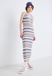 Vestido a rayas sin mangas con un escote en V profundo, que presenta líneas verticales multicolores en azul, verde y rojo. Combinado con calcetines blancos y zapatillas rosas.