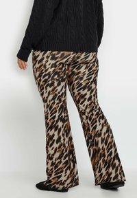 Pantaloni a zampa d'elefante con stampa leopardo, dal tocco liscio in beige, marrone e nero, abbinati a un maglione oversize a treccia nera.