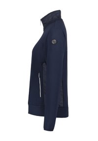 Marinblå zip-jacka med hög krage, texturerat tyg, sidofickor med kontrasterande dragkedjor och en cirkulär logotyp på ärmen.