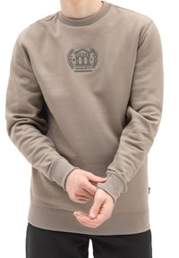 Sudadera marrón con cuello redondo, puños y dobladillo de canalé, que presenta un logotipo bordado detallado en el centro. Tejido suave y texturizado.