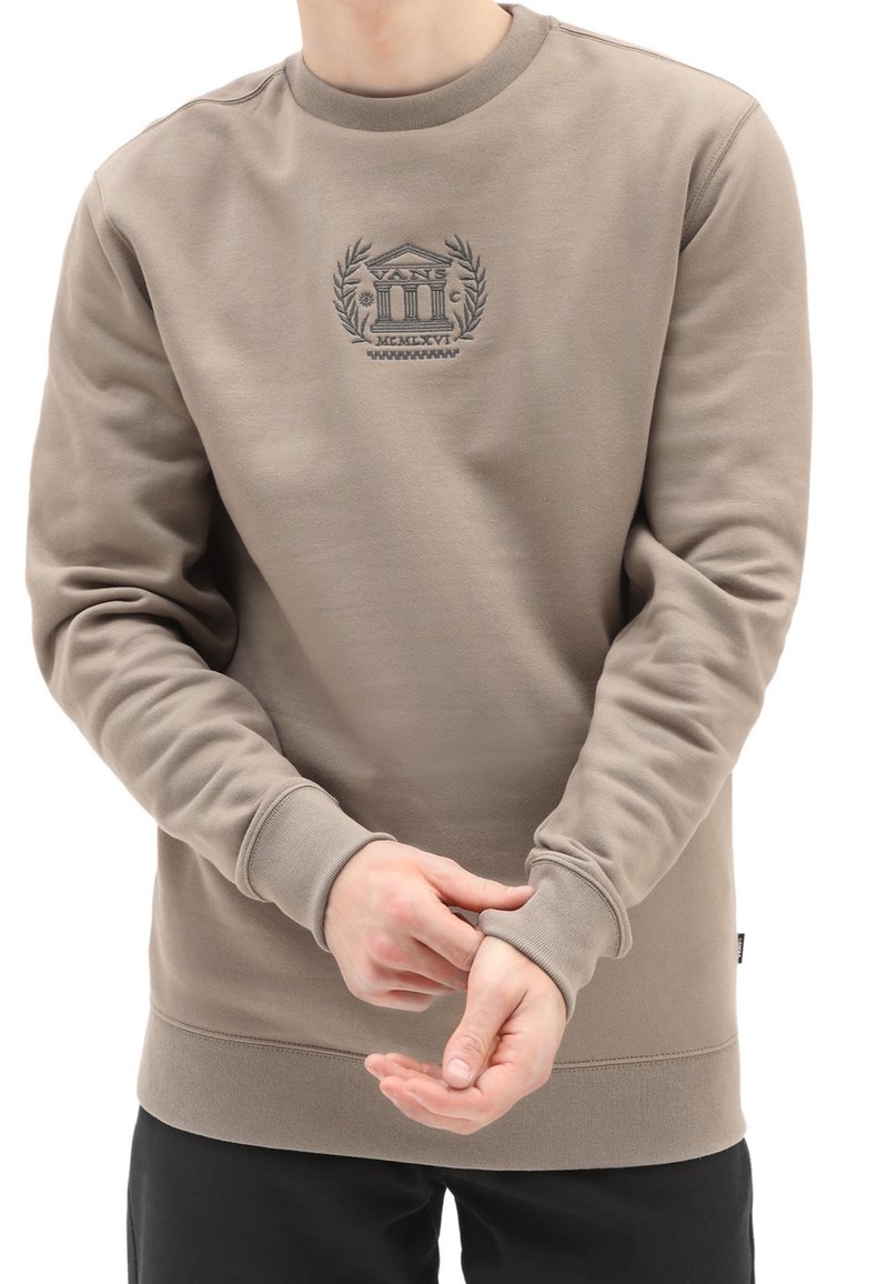 Sudadera marrón con cuello redondo, puños y dobladillo de canalé, que presenta un logotipo bordado detallado en el centro. Tejido suave y texturizado.
