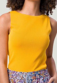 Haut jaune sans manches en tissu côtelé, avec col rond. Associé à un short à motif, taille élastiquée avec cordon de serrage.