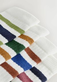 Quatre paires de chaussettes blanches en tricot empilées, chacune avec une rayure d'une couleur différente : verte, orange, bleue et rose.