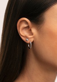 Orecchino ad anello in argento e un piccolo orecchino a forma di stella nell'orecchio. L'anello è lucido, mentre il chiodo presenta un centro in pietra preziosa trasparente.