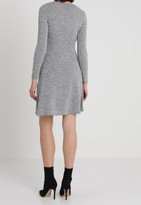 Grå långärmad klänning i mjukt tyg, med utsvängd kjol, knälång, i kombination med svarta högklackade ankelboots.