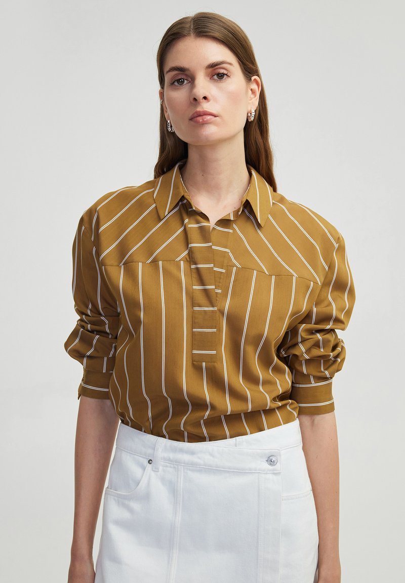 Mosterdgestreepte shirt met een knoopsluiting kraag, met witte verticale strepen en opgerolde mouwen, gecombineerd met een witte denim rok.