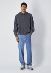 Sudadera de algodón gris oscuro con bolsillo frontal y logo, combinada con jeans holgados de mezclilla azul claro y zapatillas grises. Textura suave y diseño casual.