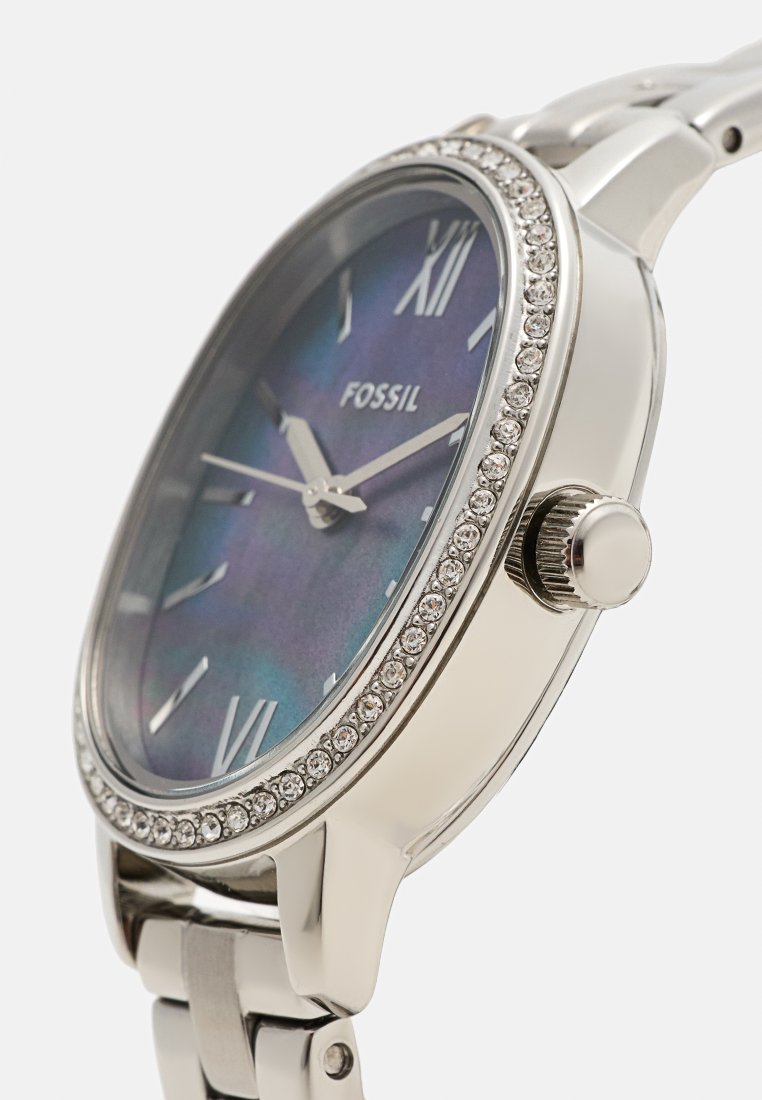Montre en acier inoxydable argenté avec un cadran irisé bleu-violet, des chiffres romains et une lunette ornée de cristaux. Dispose d'un bracelet classique en maillons.