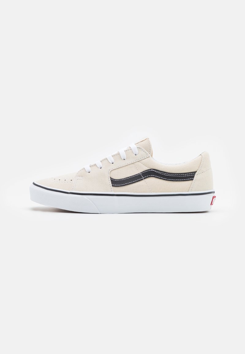Beige suede sneaker with a black side stripe, white laces, and rubber sole. Features perforations on the toe and a low-profile design.