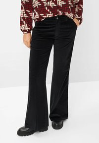 Zwarte corduroy flared broeken met verticale ribbels, voorzien van voorzakken en een enkele knoopsluiting, gecombineerd met chunky zwarte schoenen.