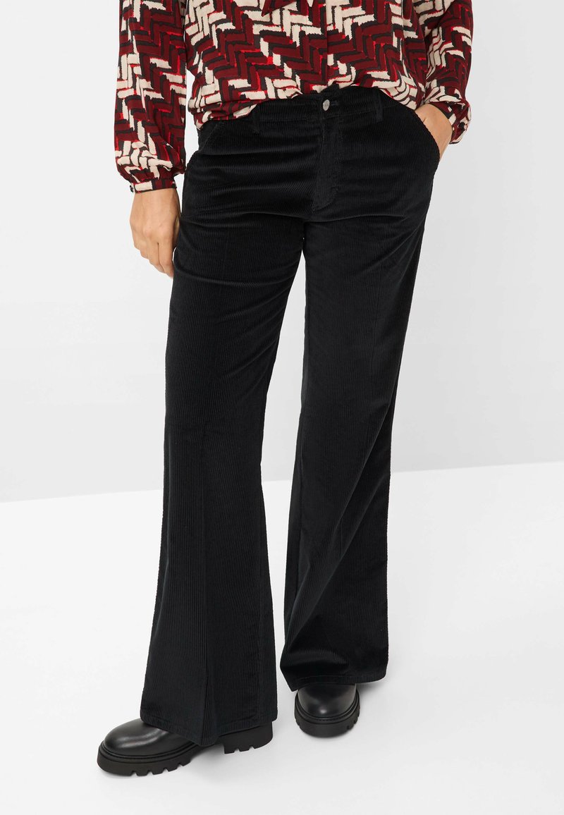 Zwarte corduroy flared broeken met verticale ribbels, voorzien van voorzakken en een enkele knoopsluiting, gecombineerd met chunky zwarte schoenen.