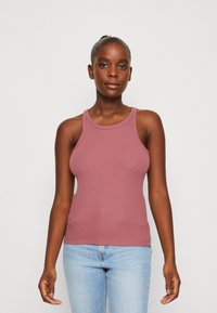 Top de tirantes acanalado en rosa empolvado, con escote redondo, tirantes anchos y silueta ajustada, combinado con jeans de un azul claro.