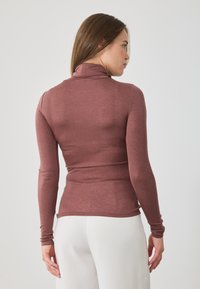 Top cu mâneci lungi și guler fals, într-o nuanță profundă de trandafir, realizat dintr-un material texturat, design ajustat care accentuează o siluetă subțire, cu mansete fără cusături.