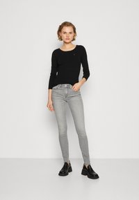 Schwarzes Langarmshirt mit Rundhalsausschnitt und geripptem Material, kombiniert mit hellgrauen Skinny Jeans und schwarzen Plateauschuhen.
