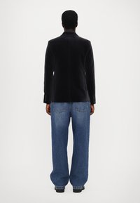 Juodas aksominis švarkas su siauru kirpimu, derinamas su per dideliais mėlynais džinsais, turinčiais užpakalines kišenes ir laisvą siluetą.