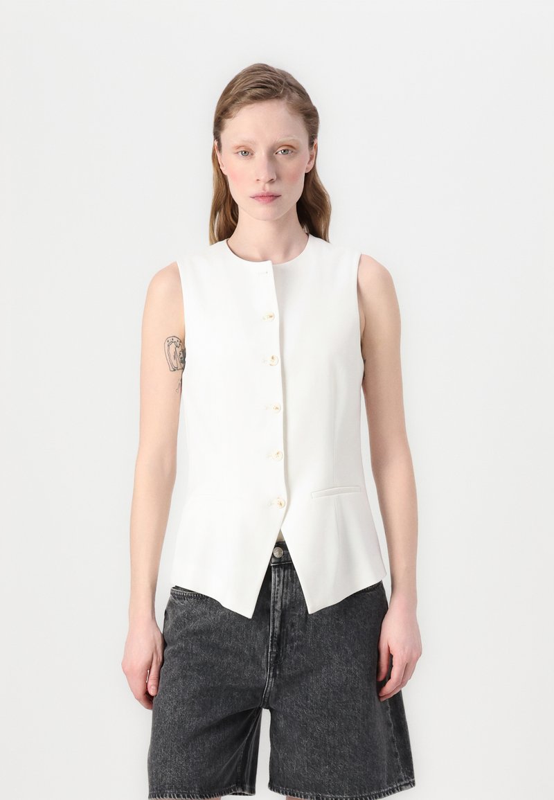 Hvit ermeløs vest med rund halslinning, seks knapper foran og spiss kant. Har et minimalistisk design og glatt tekstur.